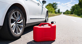 a red can of fuel next to a white car on a long road