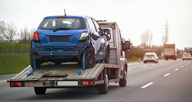 a blue car being towed on the back of a truck driving along a motorway